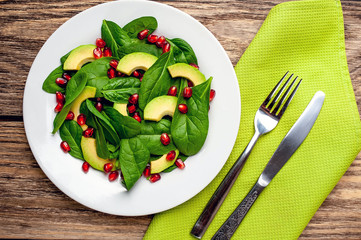 Avocado salad with baby spinach and pomegranate on a white plate on a wooden table
