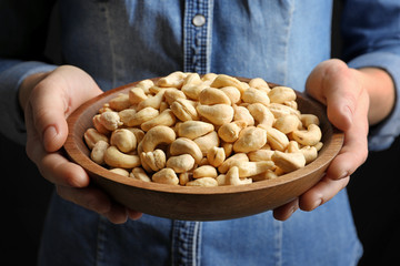 Woman holding bowl of cashew nuts on black background, closeup