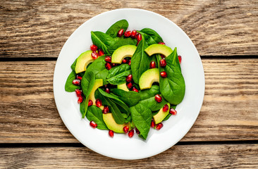 Avocado salad with baby spinach and pomegranate on a white plate on a wooden table