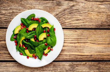Avocado salad with baby spinach and pomegranate on a white plate on a wooden table