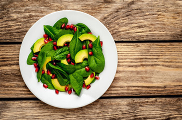 Avocado salad with baby spinach and pomegranate on a white plate on a wooden table