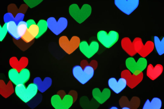 Blurred view of beautiful heart shaped lights on dark background