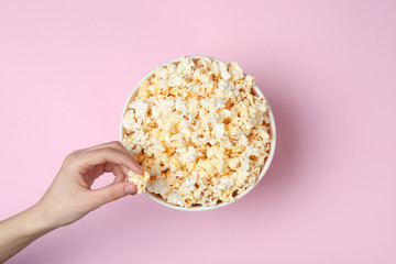 Woman eating tasty popcorn from paper bucket on color background, top view