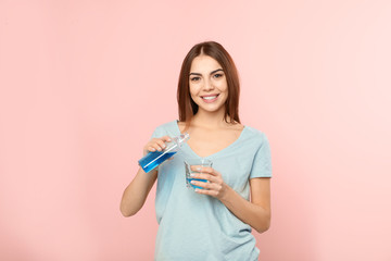 Beautiful woman pouring mouthwash from bottle into glass on color background. Teeth and oral care © New Africa