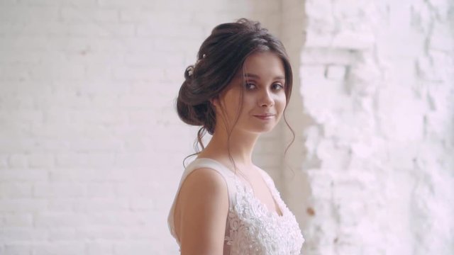 gentle image of the bride, innocent sweet girl in a long white expensive luxury dress, dark hair braided in a neat hairstyle, a modest lady smiles, stands at the big window