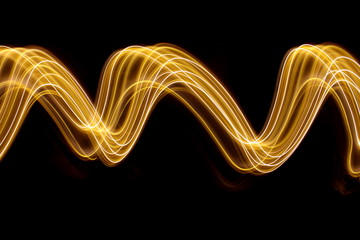 Gold light painting photography, long exposure photo of gold fairy lights in a swirling, wavy pattern against a black background
