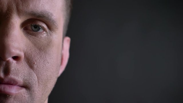 Close-up half-portrait of middle-aged caucasian man watching calmly and directly into camera on black background.