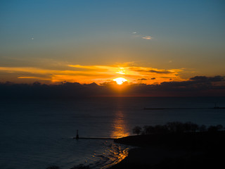 Beautiful landscape aerial photograph of colorful yellow sunrise over cumulus clouds in Chicago reflecting on the water of Lake Michigan with a pier at Foster Beach sticking out into the water below.