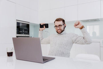 A man with glasses and a beard is happy about a good deal, sits at the computer and look at the monitor