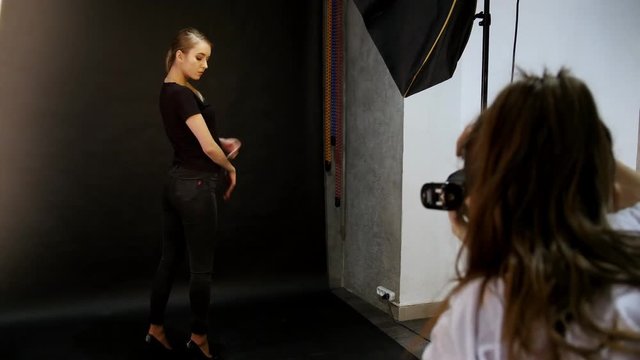 Young woman model having a photo session in the studio. Taking snaps of the model in black clothes on black background