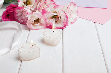 Two heart shaped burning candles and beautiful flowers on the white background