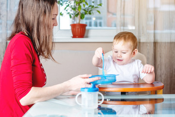 Mother feeding the baby holding hand with a spoon of food. Healthy baby nutrition. The emotions of a child while eating