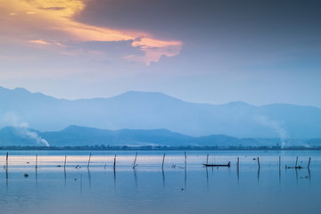 Fototapeta premium Lake view evening of a small fishing boat floating in the lake with mountain and cloudy sky background, sunset at Kwan Phayao, Phayao Province, northern of Thailand.