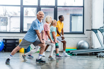happy senior multiethnic sportspeople synchronous stretching at sports hall