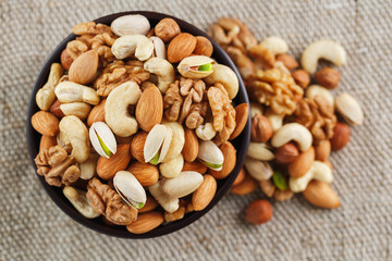 Mix of different nuts in a wooden cup against the background of fabric from burlap. Nuts as structure and background, macro. Top view.