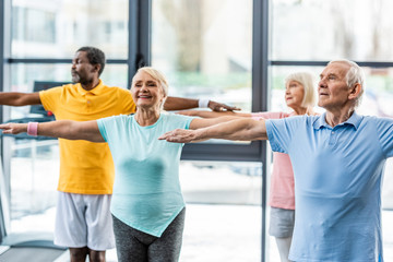Obraz premium happy multiethnic senior athletes synchronous doing exercise at sports hall