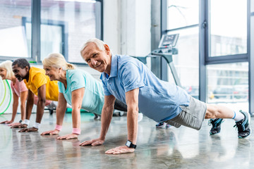 Fototapeta na wymiar happy multiethnic senior sportspeople synchronous doing plank at gym