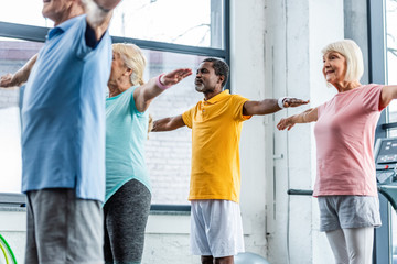 partial view of multiethnic senior athletes synchronous doing exercise at sports hall
