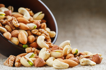 Mix of different nuts in a wooden cup against the background of fabric from burlap. Nuts as structure and background, macro. Top view.