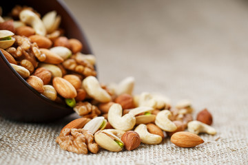 Mix of different nuts in a wooden cup against the background of fabric from burlap. Nuts as...