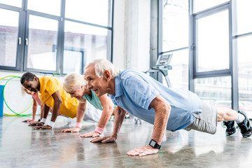 cheerful multiethnic senior sportspeople synchronous doing plank at gym