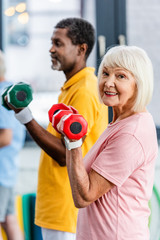 selective focus of senior woman and her african american husband doing exercise with dumbbells at...