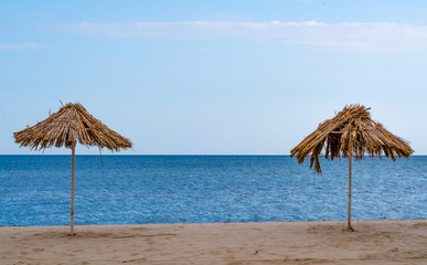 two straw beach umbrellas on an empty seashore on a clear day