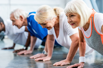 selective focus of senior sportswoman and her friends doing plank at gym