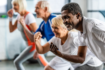 happy african american sportsman synchronous exercising with friends at sports hall