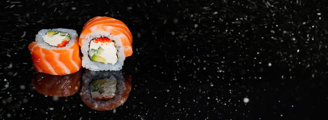 Real sushi pieces of rolls Japanese cuisine on black snow background. Chritmas. New year.