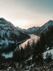 Der abenteuerlustige Mann steht oben auf dem Berg und genießt die schöne Aussicht während eines lebendigen Sonnenuntergangs. Eine Luftaufnahme eines wunderschönen Sees in Tirol, Südösterreich, bekannt als der Plansee.