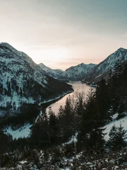 Fototapete Schwarz Der abenteuerlustige Mann steht oben auf dem Berg und genießt die schöne Aussicht während eines lebendigen Sonnenuntergangs. Eine Luftaufnahme eines wunderschönen Sees in Tirol, Südösterreich, bekannt als der Plansee.