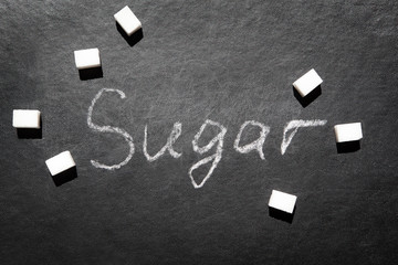 Sugar - word with white chalk on black blackboard and sugar cubes, diabetes or sweet food concept
