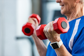 partial view of of senior sportsman with smartwatch doing exercise with dumbbells at gym