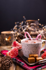 Cocoa with marshmallows in a white mug, different Christmas candies and sweets on a wooden background. Photo in dark style and free space for text. Candles and holiday decorations. 