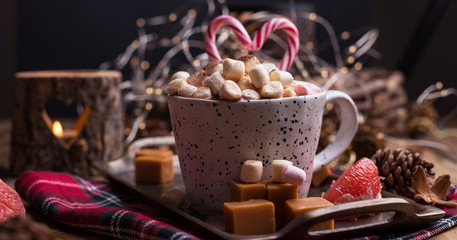 Obraz na płótnie Canvas Cocoa with marshmallows in a white mug, different Christmas candies and sweets. Photo in dark style and free space for text. Candles and holiday decorations. Postcard and greetings.