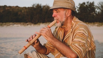 Portrait of senior man playing bamboo flute on the beach next to fishing boat © alexeg84