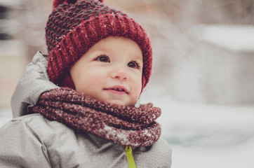 Funny little child girl wearing in red hat, a scarf, and a warm winter suit with gloves having fun...
