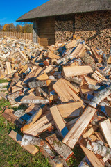 Pile and wall of cut birch wood and stacked wood logs ready for winter, standing on the grass near a Lithuanian typical wooden house