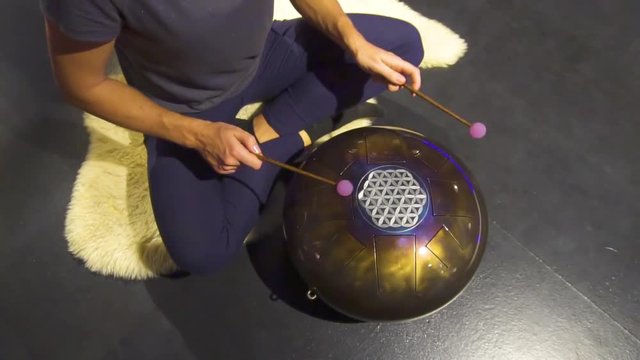 Woman is playing meditative instrument tank drum in a dark meditation room.