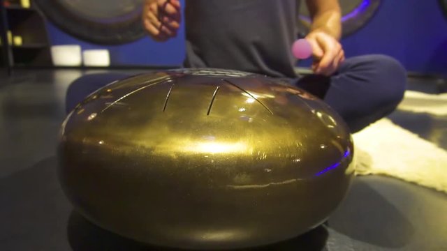 Woman is playing meditative instrument tank drum in a dark meditation room. Close-up