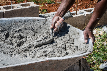 Hands of an adult black male mason scooping wet cement  from wheelbarrow using trowel. Cement block...