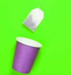 Empty disposable paper cup for tea, tea bag on green background, top view, minimalism.