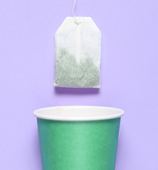 Empty disposable paper cup for tea, tea bag on violet pastel background, top view, minimalism.