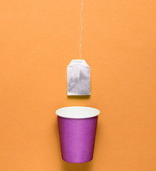 Empty disposable paper cup for tea, tea bag on orange background, top view, minimalism.