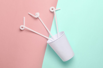 Paper coffee cup with cocktail straws on a colored pastel background, top view, minimalism..