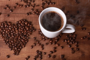 Steaming hot coffee and beans in shape of heart on vintage wooden table. Coffee break concept. White cup, Valentines day, espresso, top view