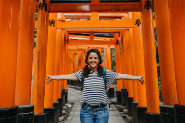 Young occidental woman doing sightseeing in the Fushimi Inari-taisha shrine in Japan. Walking the long way to the top full of red torii. Travel photography. Lifestyle.