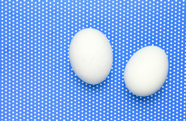 Two white chicken eggs on  blue background in polka dot. Top view.