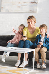 happy mother with adorable smiling kids using remote controller and watching tv together